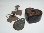 Quatro peças em metal: a) Par de porta-velas em metal dourado na forma de flores, base em forma de folha. Marcados Saretta. 6 x 10 x 9cm. b) Caixa em ferro na forma de coração, tampa ornamentada em alto relevo com volutas, empenada. 6 x 11 x 11cm. c) Prendedor de papel aplicado com Parthenon em alto relevo em uma das faces, a outra aplicada com coruja, 1967. 9 x 6cm.