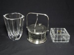 Três peças em cristal e vidro: a) ORREFORS - Vaso de flores em cristal translúcido grosso. Assinado no fundo. Bicado na borda interior. 14 x 9 x 9cm. b) Açucareiro em vidro decorado com losangos, estrutura em metal prateado com tampa e alça reclináveis, dobradiça da tampa aplicada com acantos. Marcada Prata Span. 16 x 12cm. c) CRISTAL d'ARQUES - Caixa em demi-cristal francês, moldada em blocos, selo da loja na tampa. 5 x 9 x 9cm.