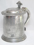 JOHN SOMMERS - Tankard em estanho polido, cinzelado no corpo com decoração de rei e rainha não identificados, pega da tampa flexionável moldada, pega em voluta. Apresenta desgastes. Marcada. 17 x 17 x 11cm.