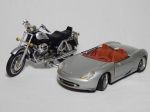 Duas miniaturas de veículos: a) Miniatura de Porsche Boxter em metal, escala 1/18, marcado Maisto. Alguns desgastes, eixo da roda frouxo. Comp. 24cm. b) Miniatura de motocicleta em plástico e resina, modelo Moto Guzzi California EV. Leves desgastes. 30 x 40cm.