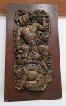 Placa para pendurar contendo escultura em pedra retratando figura mitológica pré-colombiana. Medindo: 28 cm.
