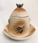 Porta mel confeccionado em faiança, com espaço para colocar água que evita a entrada de formigas, decorado com abelhas em relevo. Med. 14x14 cm.