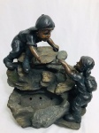 Fonte de água decorada com escultura de menino e menina na pedra, em resina. Med. 57x55 cm.