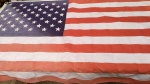 Bandeira Americana com as 50 estrelas bordadas. Mede aproximadamente 88 X 152 centímetros. Apresenta descoloração na cor azul em razão do tempo. Fabricada nos Estados Unidos da América.