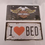 31. (2) Placas decorativas de metal, sendo uma com emblema da HARLEY-DAVIDSON. A peça traz a imagem da águia americana, representando a liberdade, e a data de fundação da companhia mais admirada pelos motociclistas, 1903, além da inscrição `AN AMERICAN LEGEND` (`Uma lenda americana`). E outra placa com a inscrição Amo Minha Cama.  Medem 30x15cm.