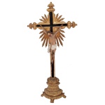 Imagem brasileira em madeira policromada e dourada, representando Cristo na Cruz. Hastes ornamentadas por frisos e ponteiras lavradas com vazados, centralizando grande adorno raiado. Base semicircular esculpida com gomos e apoiada em pés de garra. Séc. XX. 68 x 34 x 9 cm.