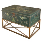 Baú em folha de flandres apresentando pintura de autoria de Erma Antunes. Superfície de fundo verde musgo com decoração de pássaros e flores. Ferragens de época. Acompanha base em ferro. 28 x 80 x 43 cm. Pertenceu ao acervo da artista plástica Linda Basto, RJ.