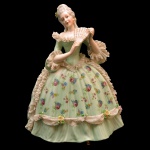 Estatueta de porcelana policromada representando figura de dama com leque e vestido com flores. Marcas da manufatura no fundo da peça. 21 x 16 x 11 cm.