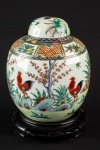 Potiche de porcelana chinesa de forma globular. Fundo de superfície branca com decoração com galos e folhagens. China. Séc. XX. 20 x 15 cm. Acompanha base de madeira.