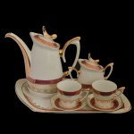 Tete a Tete em porcelana nacional. No fundo marcas da manufatura: Porcelana Schmit, Santa Catarina. Made in Brasil. Constando de: bandeja (27 x 16 cm); bule (8 cm); açucareiro (10 cm); 2 xícaras com pires (5 x 8 cm / 19 cm pires)