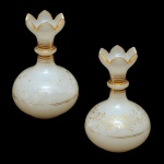 Par de vasos bojudos em opalina branca com frisos e decoração de delicadas flores em dourado. Borda em formato de pétalas. França. 14 x 10 cm. Bocal 5,5 cm. Apresenta desgastes nos frisos dourados e trincados.