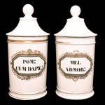 Par de potes de farmácia de porcelana francesa. Superfície branca apresentando rótulo com as inscrições: POM CUM DAP e MEL ARMUR, envolto em moldura octogonal em esmaltes azul e dourado. França. Séc. XIX. 26 cm.