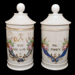 Par de potes de farmácia de porcelana francesa. Superfície branca apresentando rótulo com as inscrições: EXT: DE CAM: e PIL: INDIEN, envolto em cornucópia de cor azul com flores. França. Séc. XIX. 29 cm.