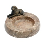 Escultura de cachorro em postura de descanso, em bronze pousado em base de mármore róseo mesclado e de forma circular. Séc. XX. 9,5 x 19 cm.