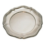 Travessa circular em prata alemã lisa, com borda ondulada e recortada, lavrada em canelados. Contraste da prata alemã de teor 835 e marca de prateiro. 129 gramas.