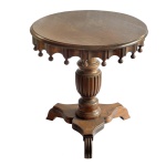 Mesa lateral de forma circular em madeira, estilo Império. Saia ondulada finalizada com bilros. Coluna central torneada finalizada em plateau com três pés. Séc. XX.  60 x 50 cm.