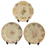 Lote composto por três pratos de porcelana alemã Bavária, sendo: A) com borda recortada e trabalho em alto relevo, em tonalidade creme, com aplicações em dourado e delicados ramos de flores nas bordas e ao centro. Manufatura: Winterling. 20 cm. B) com borda recortada, em tonalidade creme, com aplicações em dourado e delicados ramos de flores nas bordas e ao centro. Manufatura: Seltmann (1910), selo Weiden K (1949-1954). 20 cm. C) com borda lisa, aplicações em dourado e delicado ramo de flores ao centro sobre fundo creme. Manufatura: Porzellanfabrik Marktredwitz, Jaeger & Co., estampa no verso utilizada entre 1949 e 1979. 19 cm.