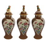 Conjunto de três potiches bojudos em porcelana chinesa da Companhia das Índias, conhecido como chocolate. Reservas centrais com decoração Família Rosa. Tampas encimada por cães de fó. China, Qing. Período Qianlong (1736-1795). 34 cm.