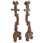 Par de tocheiros em madeira com resquícios de douração. Hastes construídas em volutas, encimadas por bobeches recortadas em metal e apoiadas em pés recurvos sobre sapatas. 75 cm. Base 20 cm.