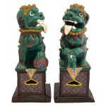 Par de esculturas chinesas em porcelana policromada representando casal de Cães de Fó, de boca aberta, sentados sobre pedestais retangulares e vazados. Apresenta-se o macho segurando o globo terrestre sob a pata esquerda e a fêmea com o filhote no colo. Bases em degraus. Séc. XIX. 52 x 22 x 23 cm.