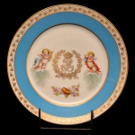 REI LOUIS PHILIPE - Raro prato de porcelana francesa de Sèvres, decorado com frisos a ouro sobre proeminente faixa azul royal, centralizando anjos e o monograma Real de Louis Philipe sob coroa. No verso marca de Sèvres e chancela do "Chateau des Tuileries". Numerado 45 com selo em vermelho ao fundo, excepcionalmente marcado com a marca suplementar representando a coroa real francesa. Séc. XIX. 23 cm.