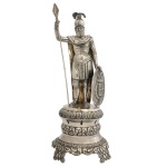 Paliteiro em prata portuguesa repuxada e cinzelada representando soldado com armadura, de pé sobre base circular ornamentada por folhagens e apoiada em pés lavrados. Contraste da cidade do Porto. Séc. XIX. Marca do prateiro José de Almeida, 1861. (Moitinho P-514 p. 283). 23 cm.