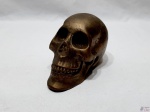 Escultura na forma de crânio humano em metal dourado. Medindo 15cm de comprimento x 9,5cm de altura.