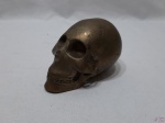 Escultura na forma de crânio humano em metal dourado. Medindo 12,5cm de comprimento x 8cm de altura.
