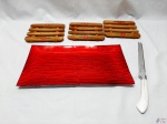 Lote diverso, composto de travessa retangular em vidro vermelho, 3 descansos de panela em madeira e 1 faca de pão/queijo. Medindo a travessa retangular 39cm x 21,5cm.