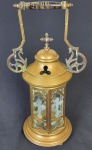 Belíssima lanterna sacra em metal dourado com alças fixas e corpo sextavado com vidros contendo imagem da cruz jateada, interior com suporte para 1 vela encimada por três pés representados por pata de leão ostentando em sua cúpula redonda crucifixo com 2 zircônias. Medindo: 39 x 21 x 13 cm.