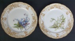 KPM - Par de pratos em porcelana polonesa na cor branca, parte central com decoração floral e ricos detalhes de ouro em alto relevo, pintados à mão.  Medindo: 18 cm.