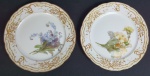 KPM - Par de pratos em porcelana polonesa na cor branca, parte central com decoração floral e ricos detalhes de ouro em alto relevo, pintados à mão.  Medindo: 18 cm.
