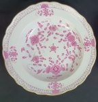 Meissen - Prato fundo em porcelana alemã, da manufatura de Meissen, esmaltado na cor rosa, com detalhes de ouro, sobre fundo branco e bordas onduladas. Medindo: 5,5 x 24 cm.