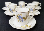 SCHMIDT - Conjunto anos 50, com seis xícaras de café acompanhada de seus respectivos pires, em porcelana esmaltada e vitrificada, delicadamente adornada com ramos florais e bordas com frisos prateados. SEM USO.