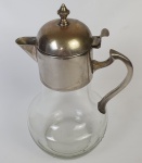 Jarra em vidro translucido com pega e tampa em metal espessurado à prata. Medindo: 22 x 15 cm.