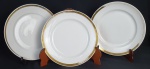 Três pratos em porcelana na cor branca com bordas em ouro. Medindo 24 cm. Apresenta desgastes na douração.
