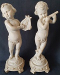 Par de querubins em resina. Medindo: 35 x 11 cm. Um com restauro na perna.