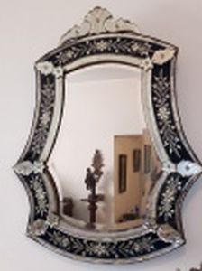 Espelho veneziano, cristal bizotado, moldura lapidada com flores e folhagens sobre fundo preto, arremates superior com volutas. Marcas do tempo. 94 x 74cm.