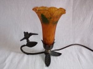 Luminária de mesa estilo Art Noveau, base em metal moldado com folhas e beija-flor, cúpula na forma de copo-de-leite em vidro fosco âmbar ao gosto de Tiffany´s. Funcionamento elétrico desconhecido. Alt. 20cm.