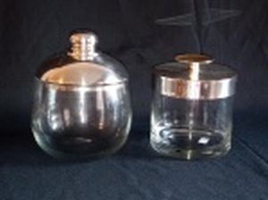Dois potes de vidro liso e translúcido, tampas de metal espessurado a prata. Alts. 16 e 14cm.