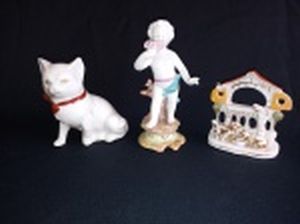 Três esculturas:  a) Em porcelana branca, representando gato com laço vermelho. Alt. 8cm. b) Em biscuit, representando menino, um dedo quebrado. Alt. 11cm. c) Representando animais em convívio, detalhes em policromia com douração. 7 x 7 x 3cm.