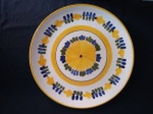 LUIZ SALVADOR - Medalhão em cerâmica vitrificada policromada com flores em amarelo, azul e verde. Pequeno bicado e fio de cabelo. Diâm. 32cm.