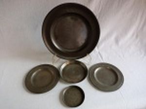 Cinco peças de estanho: sousplat, dois pratinhos, salva e porta-copos. Diferentes manufaturas. Diâm. maior 30cm, diâm. menor 10cm.