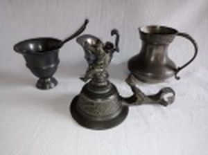 Quatro peças em estanho: 2 jarrinhas para molhos, molheira com colher e tampa de tankard ornamentada com soldado e pássaro. Maior 10cm, menor 7cm.