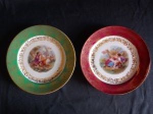 BAVARIA - Dois pratinhos decorativos em porcelana bávara, borda com cinturão azul e vermelho ricamente ornamentada por decoração floral filetada a ouro, centro aplicado com cenas galantes em policromia. Marcados no fundo. 18cm.