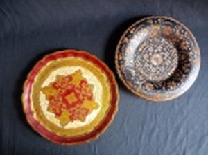 Dois pratos decorativos em madeira, sendo um ricamente policromado com vermelho e dourado, interior ornamentado com acantos e cinturão de folhas de louro, diâm. 23cm; e um com fundo preto decorado com fragmentos de placagem de madeira formando flores, diâm. 21cm.
