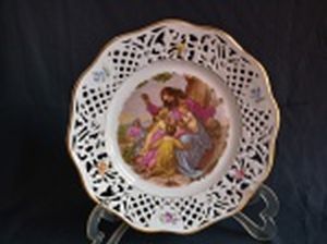 BAVARIA - Prato decorativo em porcelana alemã branca, borda filetada a ouro com galerias vazadas e decorações de flores policromadas, centro em transfer-printing aplicado com cena de crianças indo a Jesus Cristo. Marcado no fundo. Leves perdas na douração. Diâm. 23cm.
