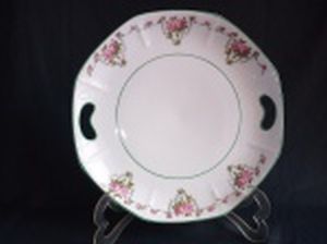 SCHMIDT - Prato com alças em porcelana nacional branca, borda e detalhes em friso verde, decoração policromada com guirlandas de rosas, formato sutilmente oitavado. Marcado no fundo. Diâm. 27cm.