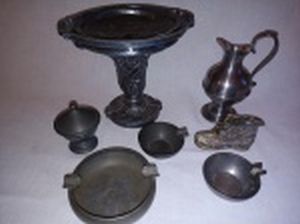 Sete peças em estanho; 3 cinzeiros redondos, 1 na forma de bota, 1 pequeno potiche, 1 ânfora polida e 1 floreira. Alt. da maior 14cm.