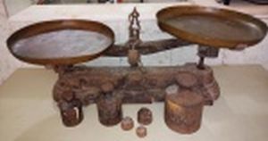 Balança dita de feira, ferro fundido, 2 pratos de metal amarelo e 6 pesos. Marca da Manufatura FILIZOLA, capacidade 30Kg. oxidada, no estado. Comp. 68cm.